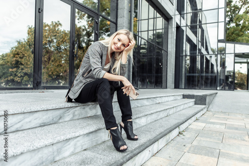 Happy Business woman sitting on the steps during the break and holding smartphone on the background of business center