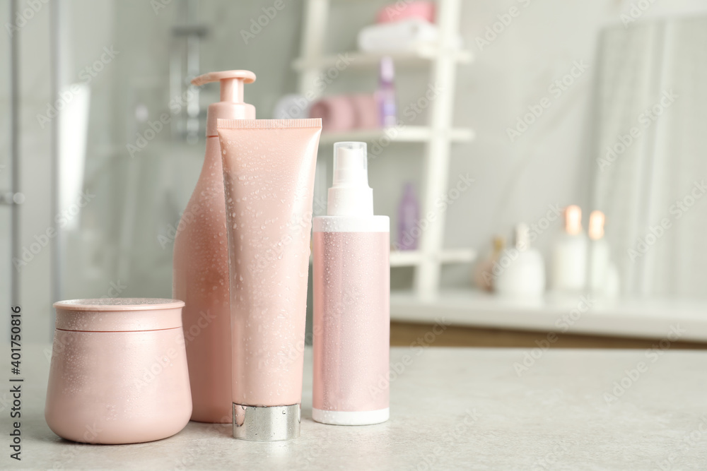 Set of hair care cosmetic products covered with water drops on light grey stone table in bathroom. Space for text Set of hair care cosmetic products covered with water drops on light grey stone table in bathroom. Space for text