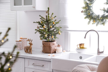Small Christmas tree decorated with baubles and festive lights in kitchen