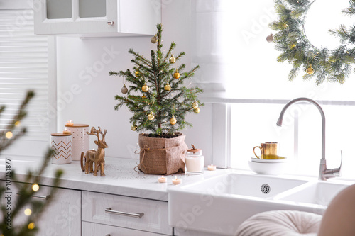 Small Christmas tree decorated with baubles and festive lights in kitchen