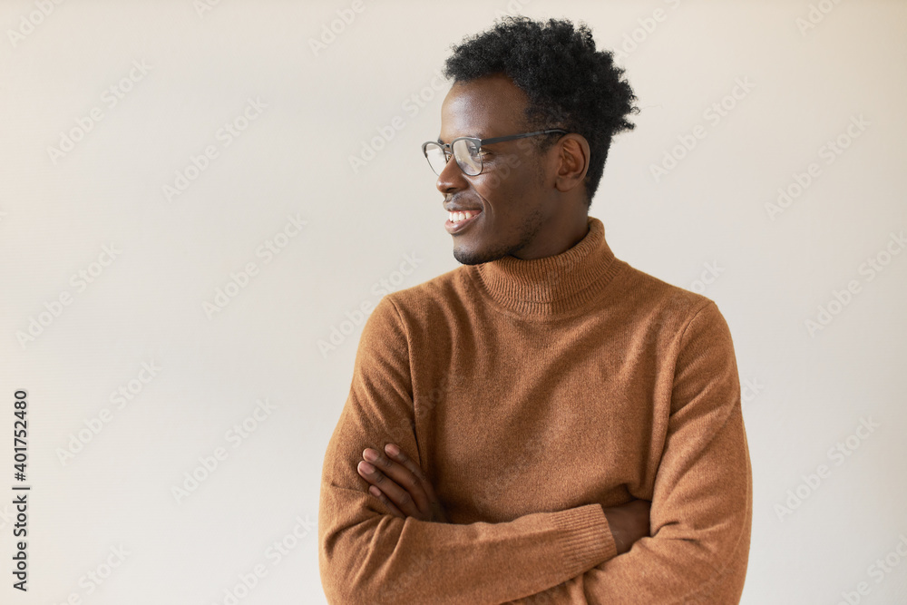 Obraz premium Body language. Horizontal shot of fashionable young African American man with stubble folding arms and looking away with confident happy smile, his look expressing confidence and optimistic attitude
