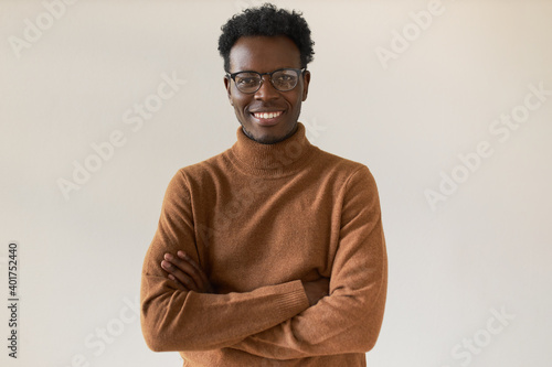 Isolated image of attractive successful young black businessman in stylish turtleneck and spectacles crossing arms and looking at camera, having confident facial expression after signing contract © Anatoliy Karlyuk