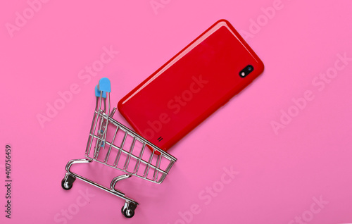 Mini shopping trolley with smartphone on pink background. Top view