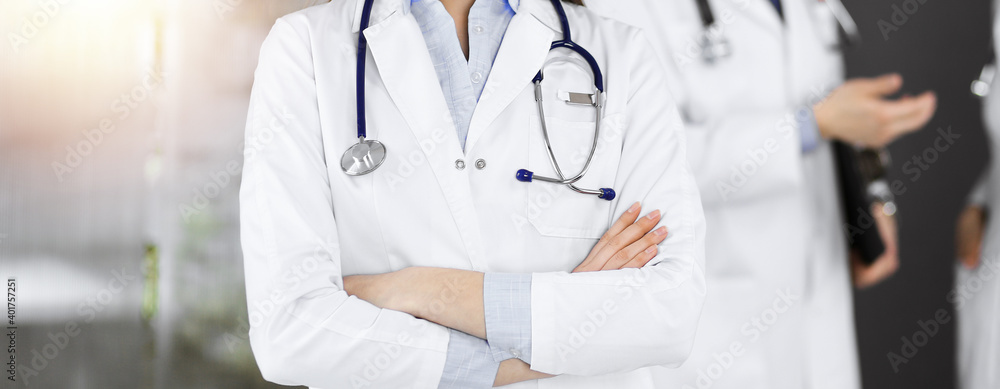 Unknown young woman doctor is standing with arms crossed in sunny clinic. Medicine concept during Coronavirus pandemic. Covid-2019 Unknown young woman doctor is standing with arms crossed in sunny clinic. Medicine concept during Coronavirus pandemic. Covid-2019