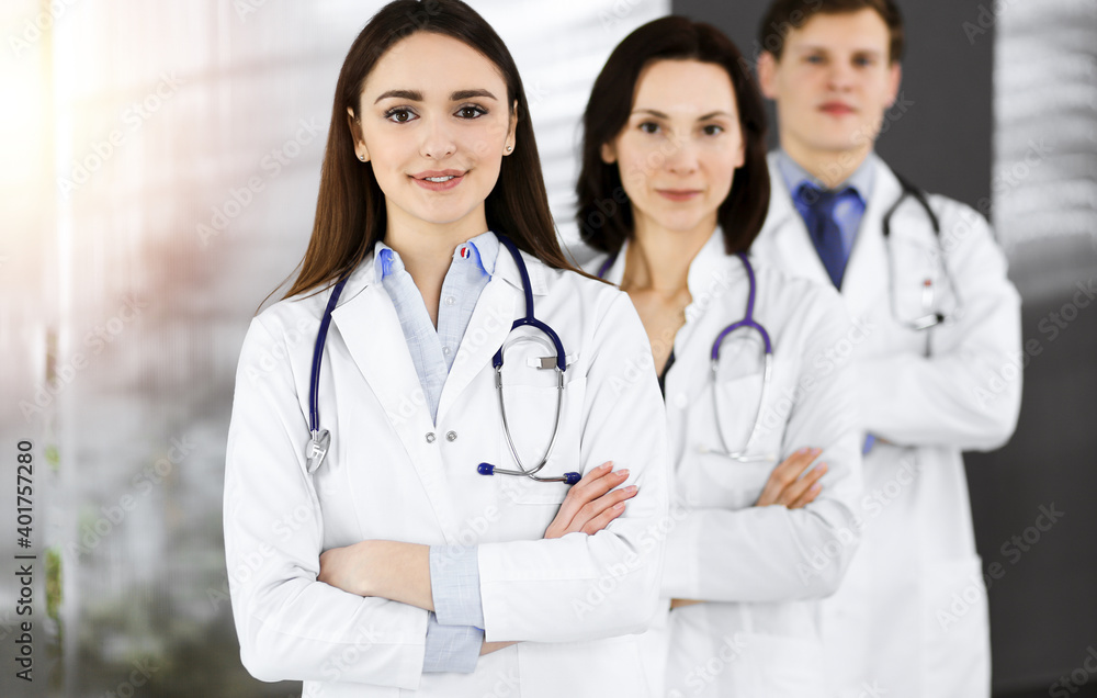 Group of young professional doctors standing as a team with arms crossed in sunny hospital. Medical help, insurance in health care, best disease treatment and medicine concept Group of young professional doctors standing as a team with arms crossed in sunny hospital. Medical help, insurance in health care, best disease treatment and medicine concept