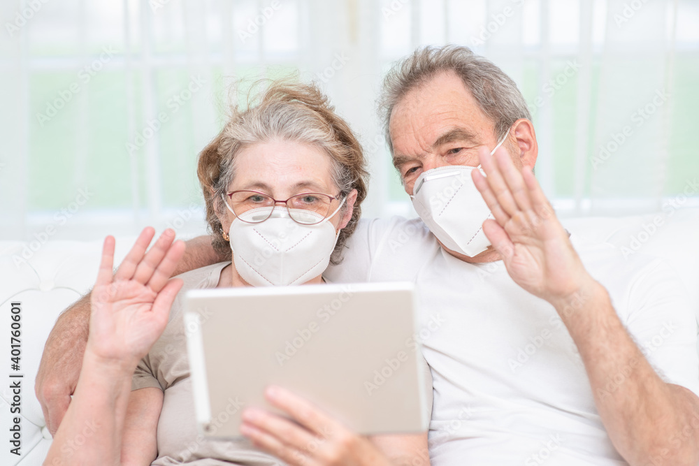 Senior couple wearing protective masks having video chat with their relatives on tablet computer during the coronavirus epidemic
