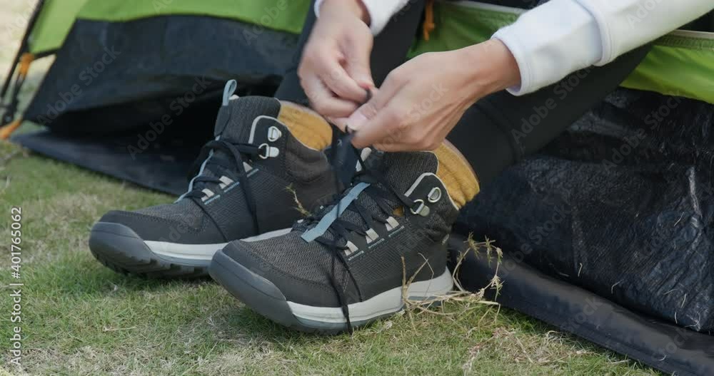 Woman tying her shoes after hiking at camping site Woman tying her shoes after hiking at camping site