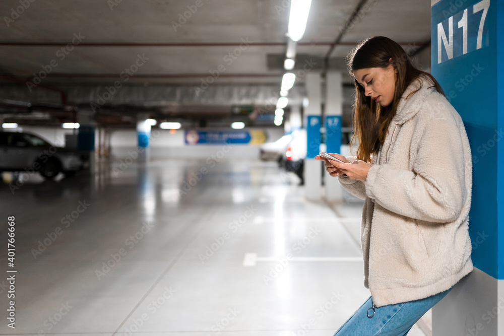 Fashionable girl with mobile phone in underground parking. Woman is texting online