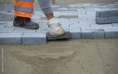 A worker in mittens lays out paving slabs on the sand.Construction of a Parking lot for cars.