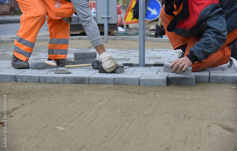 Two workers are laying paving slabs, building a parking lot for cars. Two workers are laying paving slabs, building a parking lot for cars.