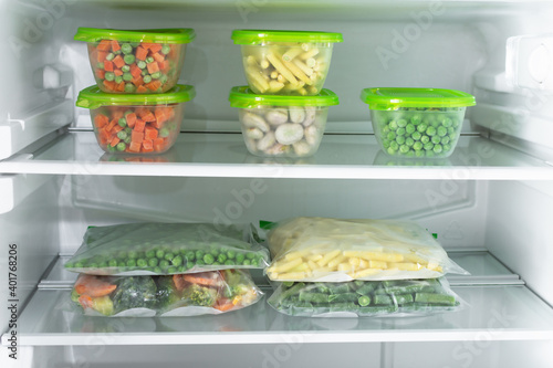 Plastic containers and bags with different frozen vegetables in refrigerator.