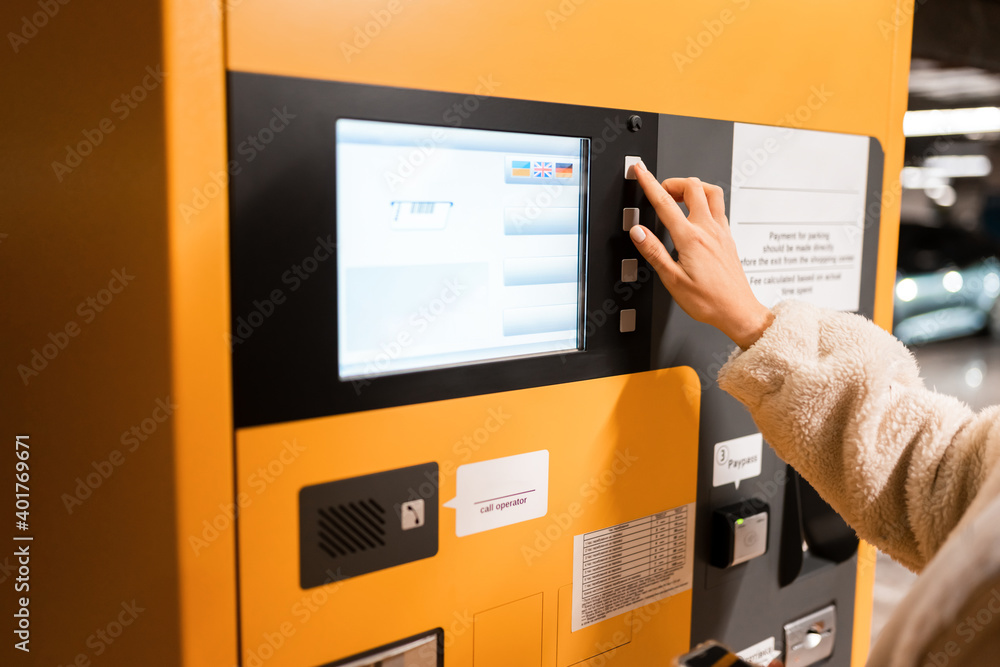Female hand presses button on a parking payment terminal. Elegant young girl pays for ticket in parking meter. Woman near terminal in the underground parking Female hand presses button on a parking payment terminal. Elegant young girl pays for ticket in parking meter. Woman near terminal in the underground parking