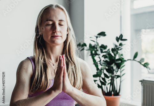 Young attractive woman practicing yoga, sitting in Padmasana, exercise, Lotus pose, namaste, working out, wearing sportswear, near floor window