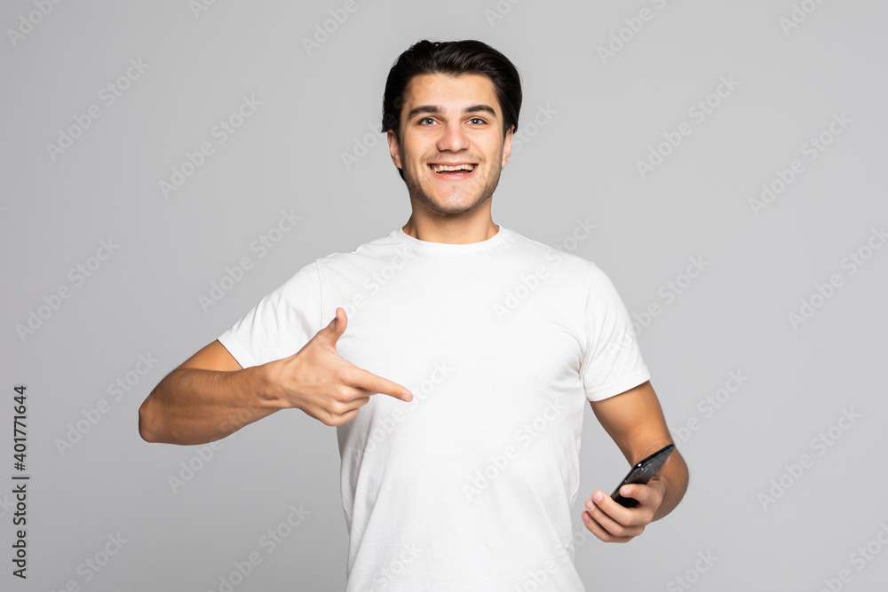 Hansome man isolated on grey background, presenting smart phone and pointing with finger at blank black screen with copyspace for ads
