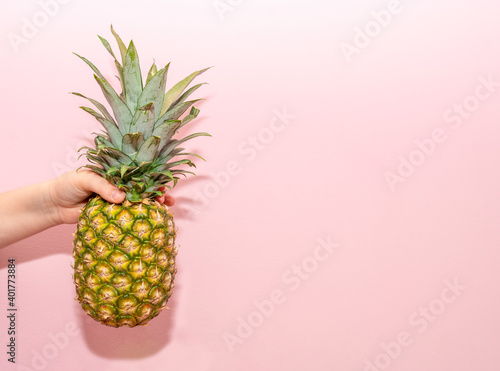 Close-up photo of a young boy holding fresh, ripe pineapple fruit in his hands isolated on a pink wall background in the studio. Appropriate healthy nutrition, vitamin concept. Trial copy space