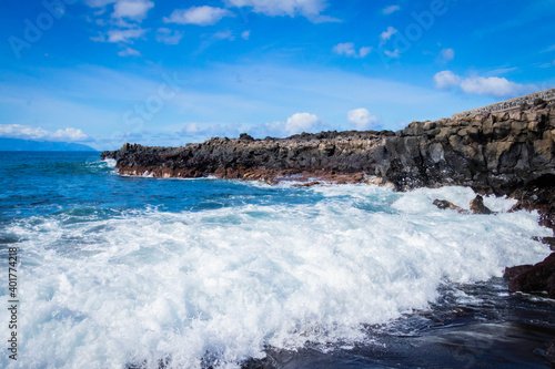  turquoise ocean breaking waves against black beach and black rocks on a beautiful sunny day