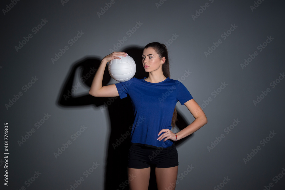 Volleyball girl hold and kick ball in blue costume on dark wall background. Player doing sport workout at home. Sport and recreation concept Volleyball girl hold and kick ball in blue costume on dark wall background. Player doing sport workout at home. Sport and recreation concept