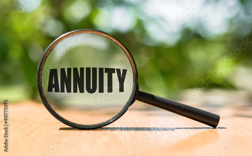 Magnifying glass with text ANNUITY on wooden table and green background. photo