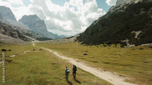 A couple hiking along a pathway leading through a valley in Italian Dolomites. High, sharp mountains around. Stony and raw landscape, green meadow. Remote and desolate place. Freedom of exploration photo