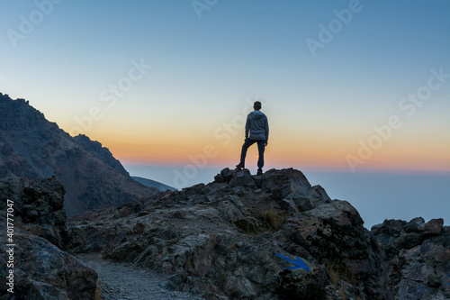 A tourist standing on the peak of a rocky mountain watching sun rising in Darband valley in autumn in dawn against colorful sky in the Tochal mountain.