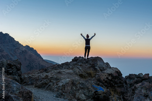 A female tourist standing on the peak of a rocky mountain watching sun rising in Darband valley in autumn in dawn against colorful sky in the Tochal mountain. © zz3701