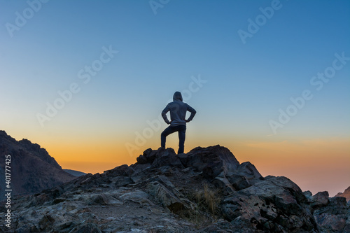 A male tourist standing on top of rocky mountain watching sun rising in Darband valley in autumn in dawn against colorful sky in the Tochal mountain.