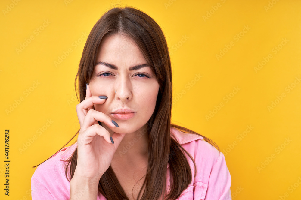 Portrait of brunette girl with doubting facial expression holds chin and squints in disbelief, makes decision isolated on yellow background Portrait of brunette girl with doubting facial expression holds chin and squints in disbelief, makes decision isolated on yellow background