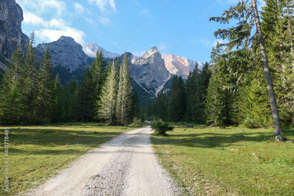 A gravelled pathway leading through a valley in Italian Dolomites. High and sharp mountains around. The slopes and meadow are green, higher parts barren and stony. Remote and desolate place. Serenity