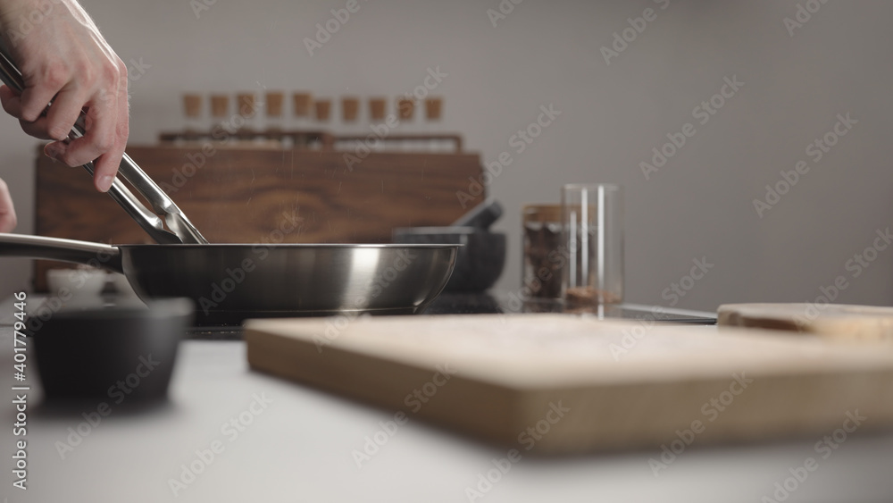 Man flip beef steak with tongs on steel pan on electric hob on kitchen Man flip beef steak with tongs on steel pan on electric hob on kitchen