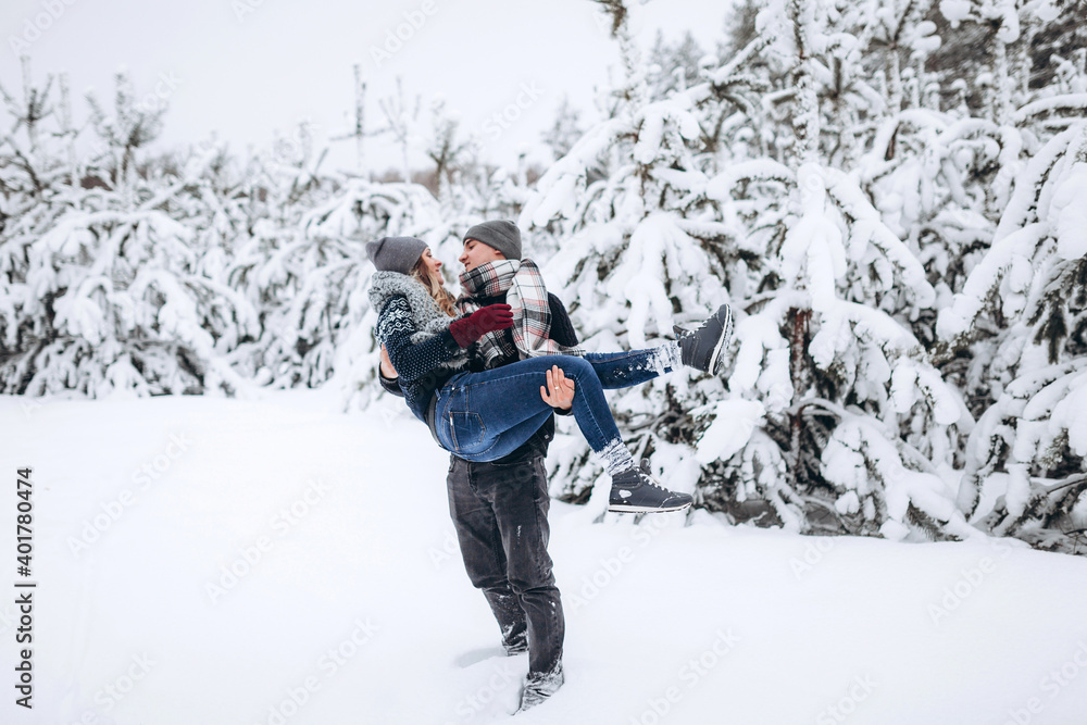 The guy holds the girl in his arms in the snowy winter forest