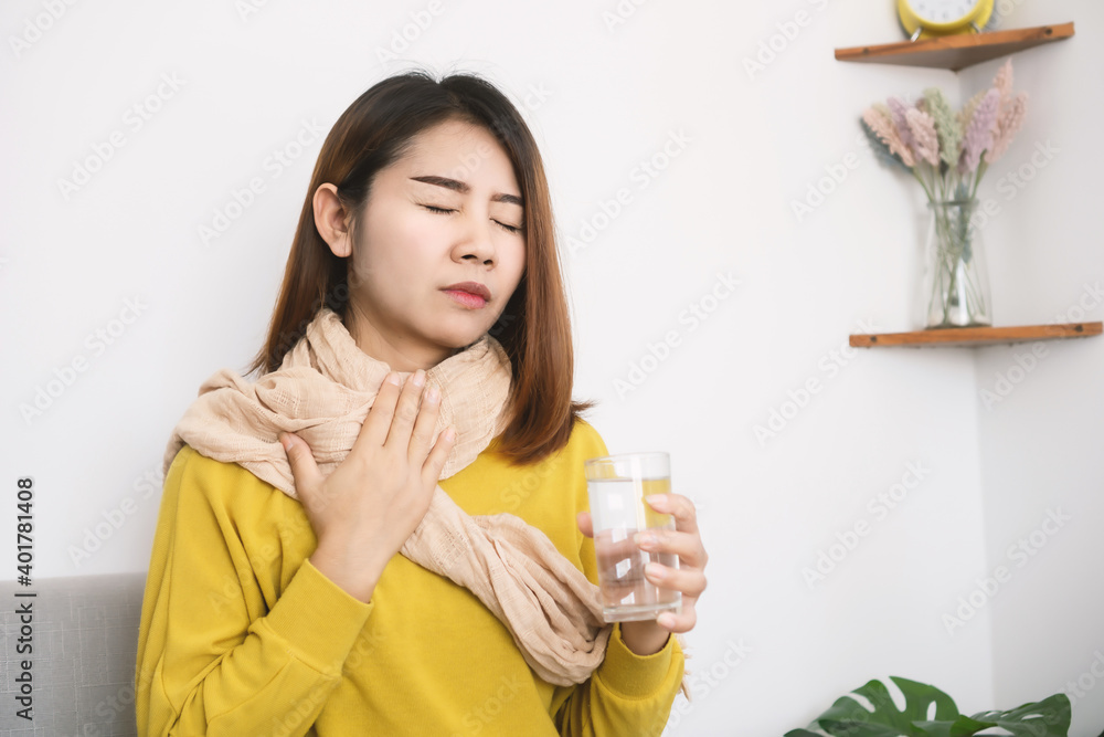 sick Asian woman suffering from sore throat hand holding glass of hot water sick Asian woman suffering from sore throat hand holding glass of hot water