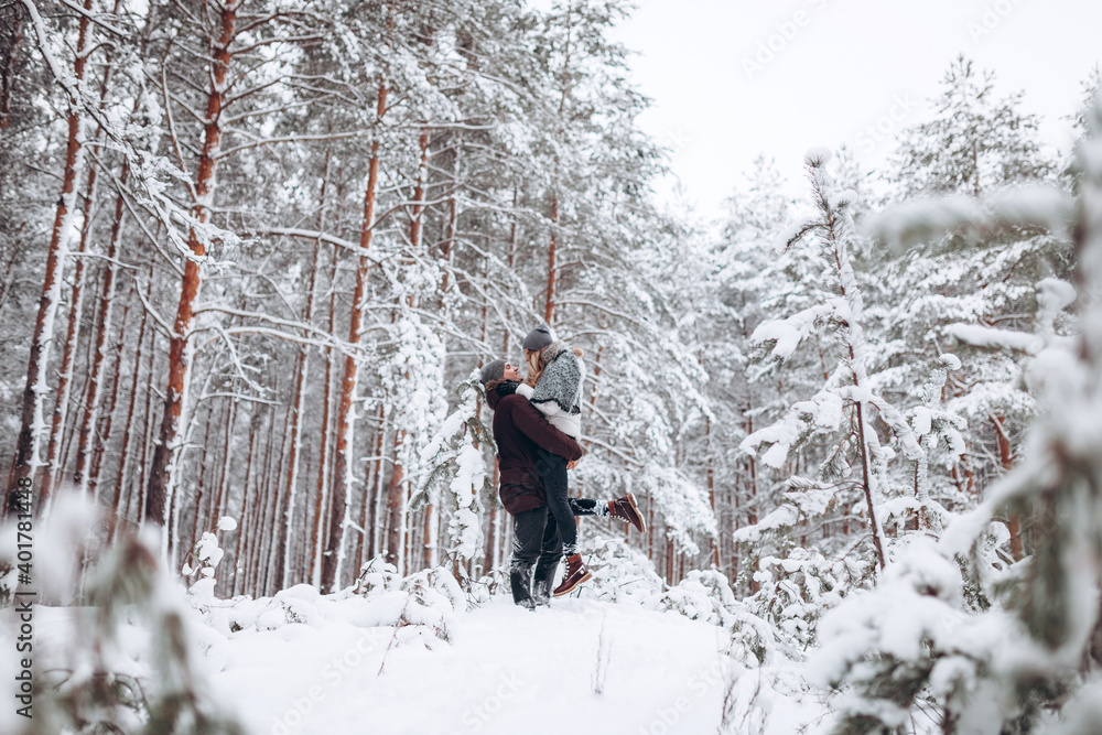 Loving young couple walks in a beautiful snowy forest in winter
