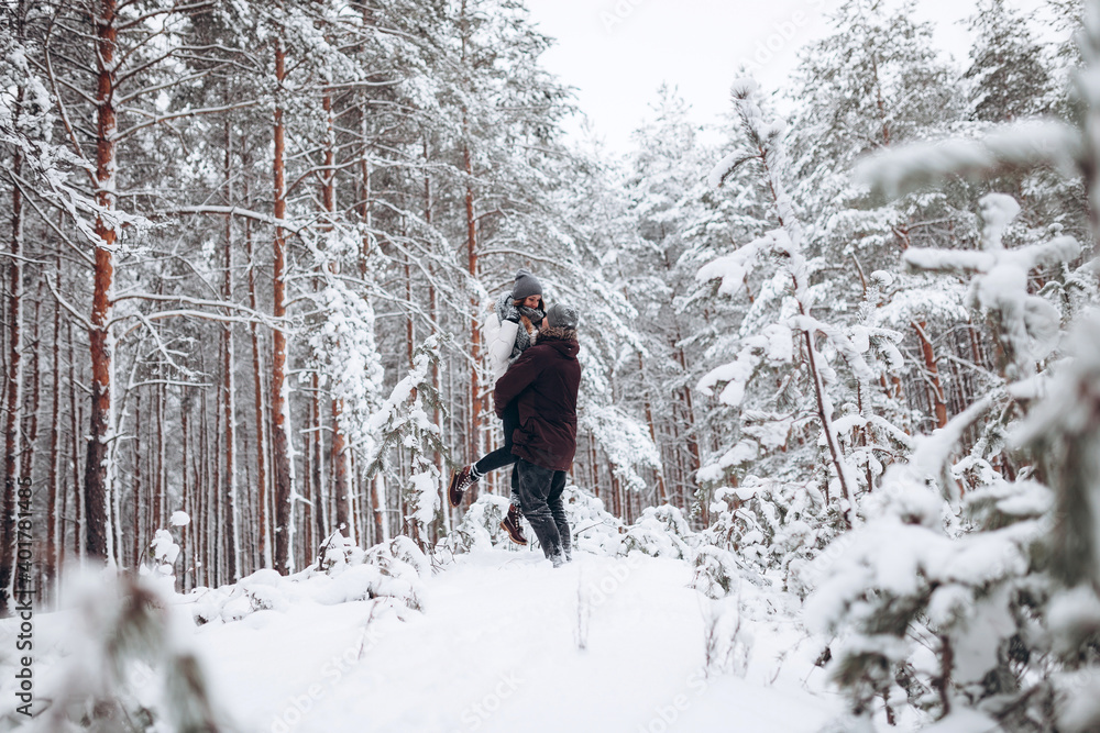 Loving young couple walks in a beautiful snowy forest in winter Loving young couple walks in a beautiful snowy forest in winter