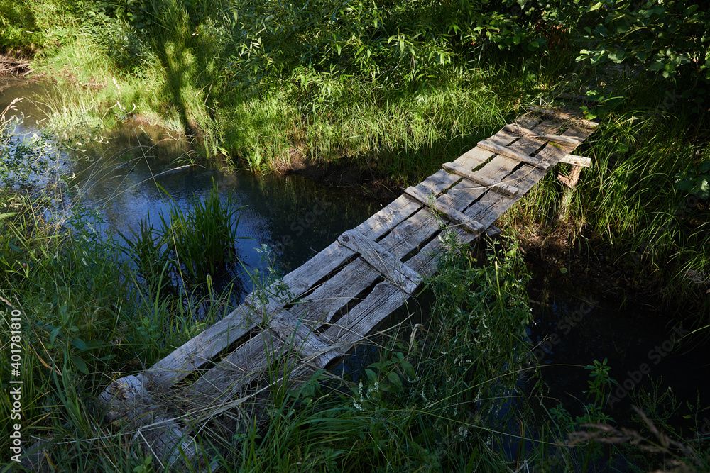Fototapeta premium A homemade bridge made of gray old boards across the river in a Russian village in summer on a sunny day