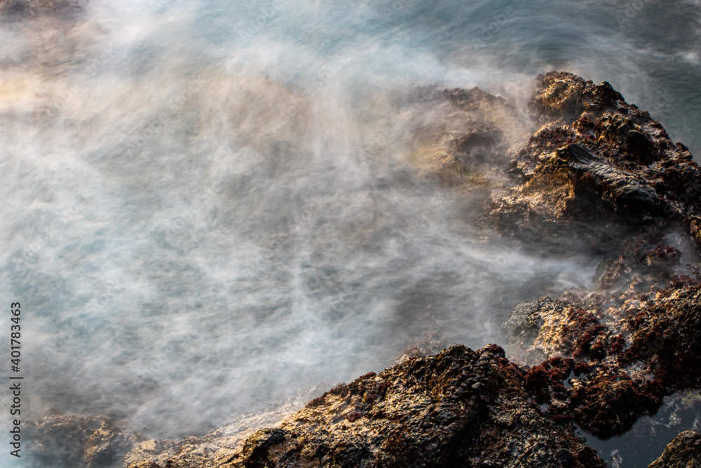 Sunset seascape with sea water in motion blur, stones on the beach. Atlantic ocean, Tenerife island. Long exposure. Background