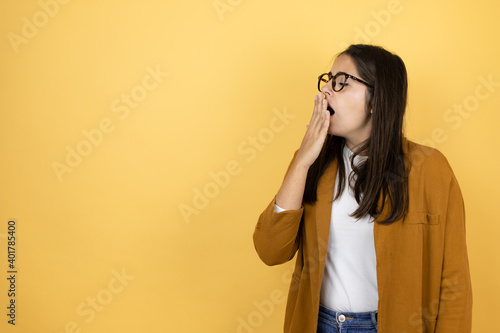 Young beautiful woman wearing a blazer over isolated yellow background bored yawning tired covering mouth with hand. Restless and sleepiness.