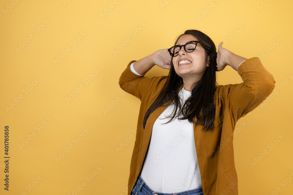 Young beautiful woman wearing a blazer over isolated yellow background relaxing and stretching, arms and hands behind head and neck smiling happy Young beautiful woman wearing a blazer over isolated yellow background relaxing and stretching, arms and hands behind head and neck smiling happy