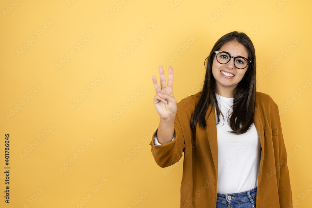 Young beautiful woman wearing a blazer over isolated yellow background showing and pointing up with fingers number three while smiling confident and happy Young beautiful woman wearing a blazer over isolated yellow background showing and pointing up with fingers number three while smiling confident and happy