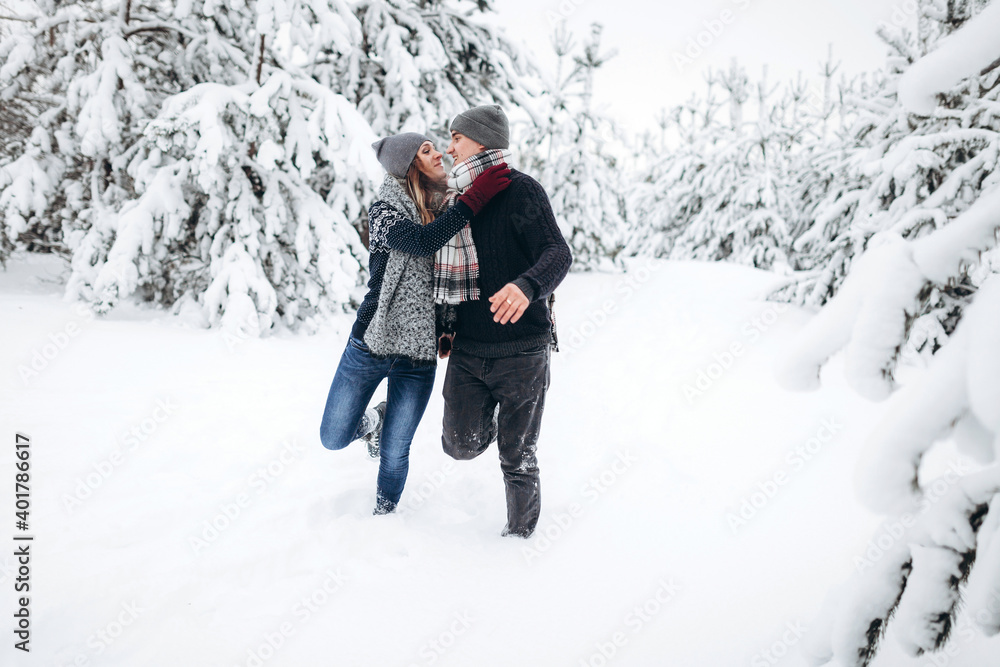 Loving couple runs through a snowy forest in winter in a sweater and a scarf and smiles
