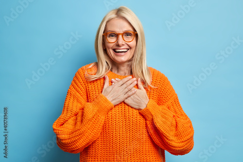 Картината върху платно Portrait of blonde female with cheerful expression keeps hands pressed to chest