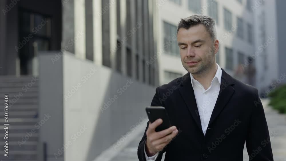 Cheerful handsome man in formal outfit dailing number and talking while having call. Ceo executive in 40s smiling while having conversation on smartphone and walking at street. Cheerful handsome man in formal outfit dailing number and talking while having call. Ceo executive in 40s smiling while having conversation on smartphone and walking at street.