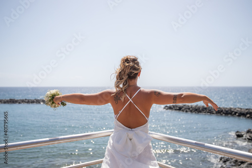 Fototapeta Naklejka Na Ścianę i Meble -  Neo bride posing with arms outstretched looking at the ocean
