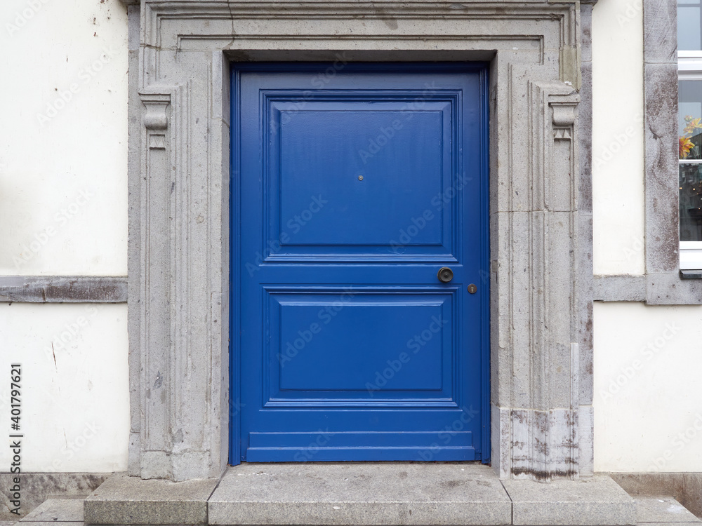 Old, blue wooden entrance door with a round handle and peephole. Historic building with white facade in the old town of Germany. Old, blue wooden entrance door with a round handle and peephole. Historic building with white facade in the old town of Germany.