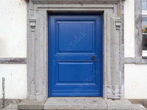 Old, blue wooden entrance door with a round handle and peephole. Historic building with white facade in the old town of Germany.