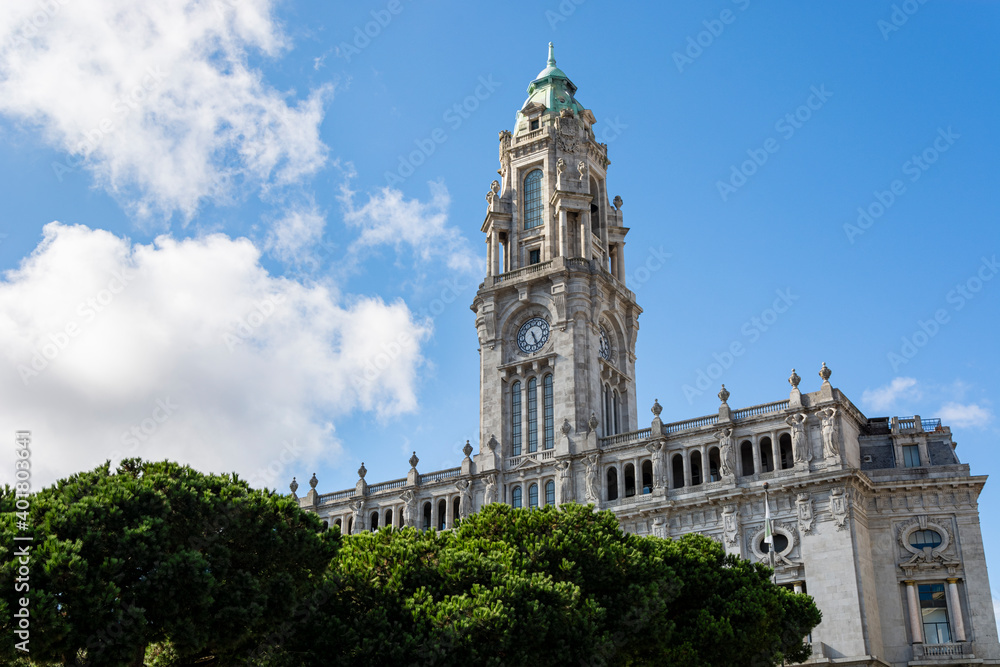 Porto City Hall. Old building with tower and clock. Pine trees in the foreground. Blue sky with clouds.