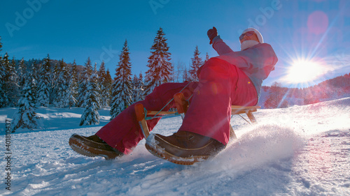LENS FLARE: Joyful woman sleds down snowy hill in the sunny Slovenian mountains.