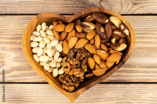Natural nutritional blend of various nuts in a wooden plate in the shape of a heart symbol on a brown wooden table. A mixture of walnuts, brazil nuts, peanuts and almonds. Healthy natural food concept