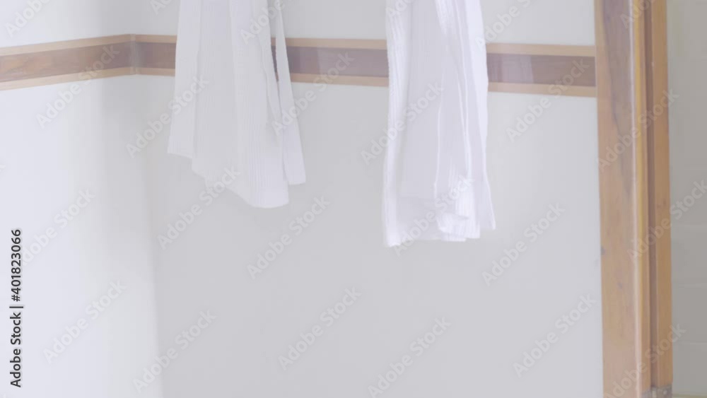 Two white robes hanging on a white wall of a hotel bathroom. Two white robes hanging on a white wall of a hotel bathroom.
