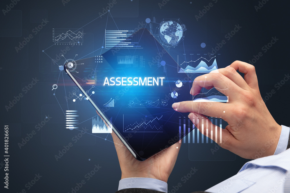 Businessman holding a foldable smartphone with ASSESSMENT inscription, successful business concept Businessman holding a foldable smartphone with ASSESSMENT inscription, successful business concept