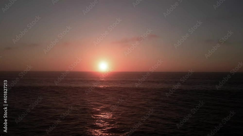 Hazy golden sun sits just above a panoramic horizon as waves roll in, aerial track Hazy golden sun sits just above a panoramic horizon as waves roll in, aerial track